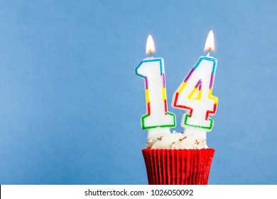 Number 14 birthday candle in a cupcake against a blue background