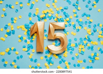 Number 15 fifteen golden celebration birthday candle on yellow and blue confetti Background. fifteen years birthday. concept of celebrating birthday, anniversary, important date, holiday