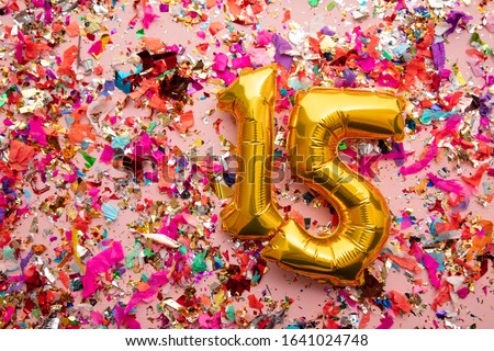 Number 15 gold birthday celebration balloon on a confetti glitter background