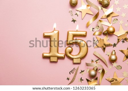 Number 15 gold celebration candle on star and glitter background