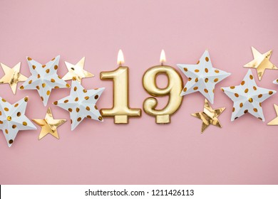 Number 19 gold candle and stars on a pastel pink background
