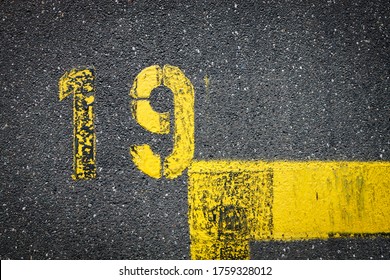 The Number 19 Nineteen Is Painted On The Asphalt With Yellow Color Thermoplastic Road Marking Paint. Marked Parking Space Delineated By Road Surface Markings, Space For Text, No People
