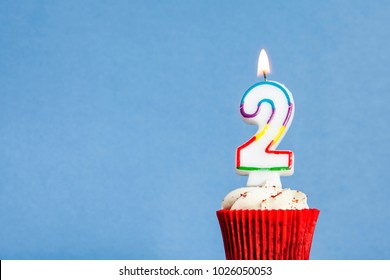 Number 2 birthday candle in a cupcake against a blue background