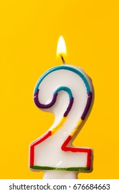 Number 2 birthday celebration candle against a bright yellow background