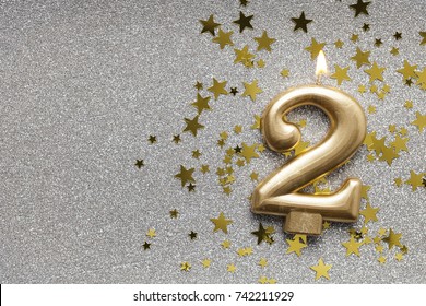 Number 2 gold celebration candle on star and glitter background