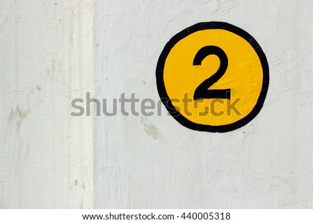 Number 2 sign painted on a white wall in yellow and black color
