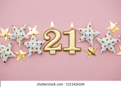 Number 21 gold candle and stars on a pastel pink background - Powered by Shutterstock