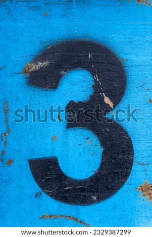 Number 3 in black paint on an old blue iron surface with rust texture and traces of dirt.