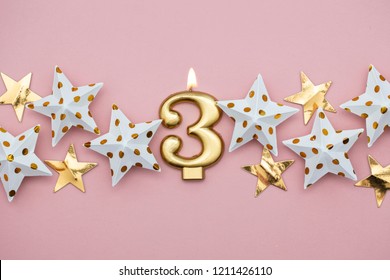 Number 3 gold candle and stars on a pastel pink background