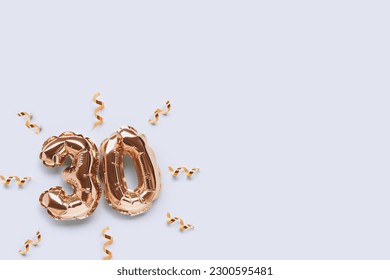 Number 30 golden inflatable balloons with ribbons confetti on a blue pastel background. Place for text.