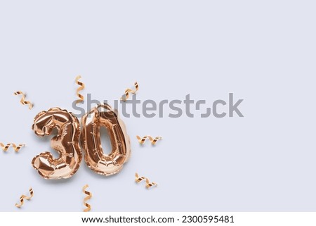 Number 30 golden inflatable balloons with ribbons confetti on a blue pastel background. Place for text.