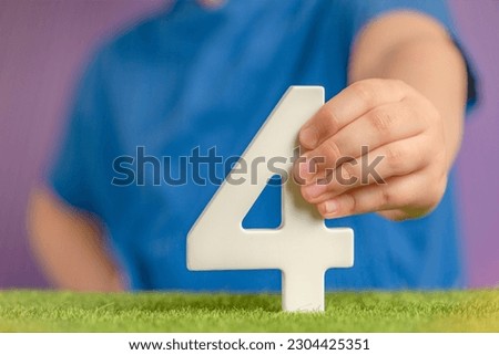 Number 4 in hand. Hand holding white number four over green grass and purple background, birthday concept, competition place, four percent per annum. Canada National Day, USA Independence Day, 4 July.