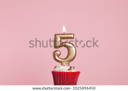 Number 5 gold candle in a cupcake against a pastel pink background