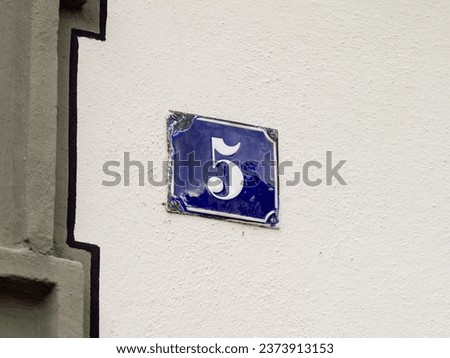 Number 5 on an exterior house wall. The metal plate is enameled and in blue color. The design very vintage and retro. The five is also a prime number.
