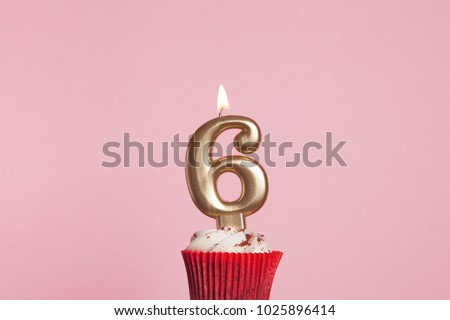 Number 6 gold candle in a cupcake against a pastel pink background