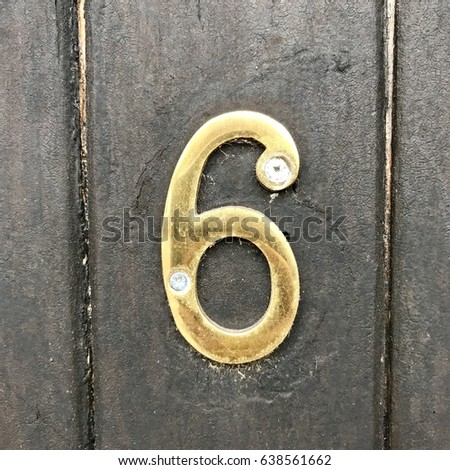 Number 6 gold metal house address number sign screwed into painted black wood fence gate door textured background