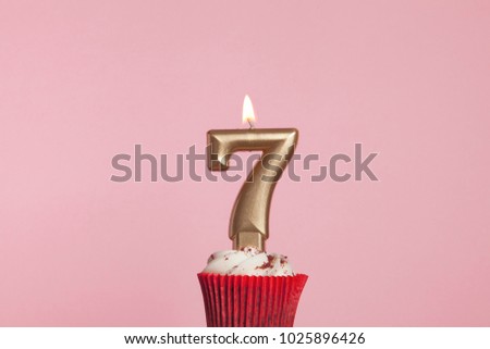 Number 7 gold candle in a cupcake against a pastel pink background
