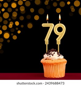 Number 79 birthday candle - Cupcake on black background with out of focus lights