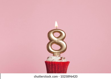 Number 8 gold candle in a cupcake against a pastel pink background