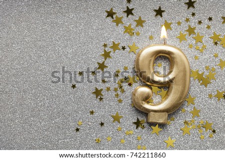 Number 9 gold celebration candle on star and glitter background