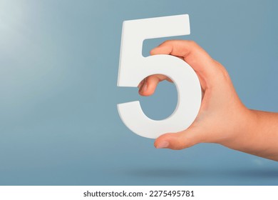 Number five in hand. Hand holding white number 5 on blue background with copy space. Concept with number five. Birthday 5 years, fifth grade, five day work week - Shutterstock ID 2275495781