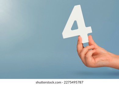 number four in hand. Hand holding white number 4 on blue background with copy space. Concept with number four. Birthday 4 years, fourth grade, four day work week