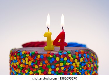 Number fourteen candle lit on top of a chocolate confetti cake