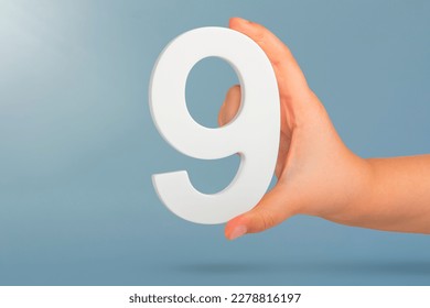 Number nine in hand. A hand holds a white number 9 on a blue background. Concept with number nine. Birthday 9 years, percentage, ninth grade or day.