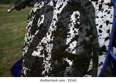 The number plate off of a bike covered in dirt.