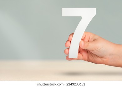 Number seven in hand. Hand holding white number 7 on blurred background with copy space. Concept with number seven. Birthday 7 years, percent, seventh grade or day.