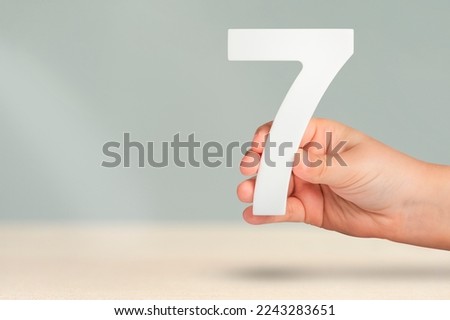 Number seven in hand. Hand holding white number 7 on blurred background with copy space. Concept with number seven. Birthday 7 years, percent, seventh grade or day.
