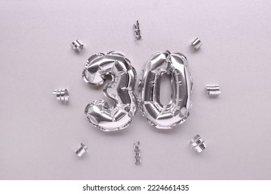 Number thirty inflatable balloons with ribbons confetti on a silver shiny background.