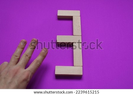 number three written with wood blocks on purple background and number 3 indicated by finger. number representation in sign language