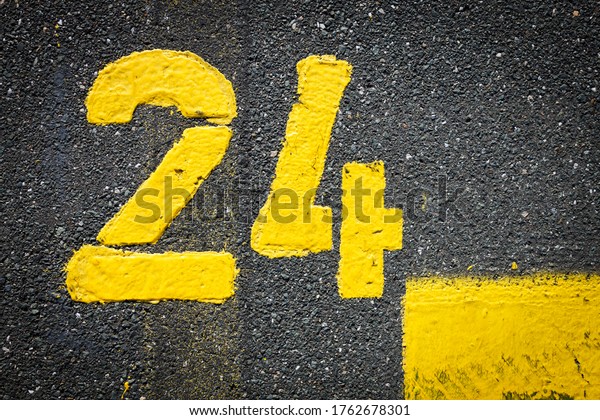 The\
number twenty four 24 is painted on the asphalt with yellow color\
thermoplastic road marking paint. Marked parking space delineated\
by road surface markings, space for text, no\
people\
