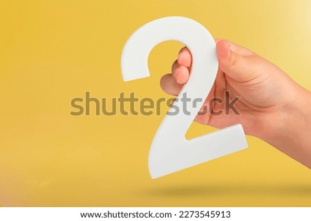 Number two in hand. Hand holding white number 2 on yellow background with copy space. Concept with number two. 2 percent, birthday 2 years old, couple, two, double