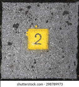 Number Two Written In A Yellow Square On Grey Brick Ground. 