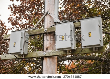 Numbered electrical junction boxes mounted on a wooden utility pole with cables and autumn foliage in the background, part of outdoor power infrastructure. High quality photo