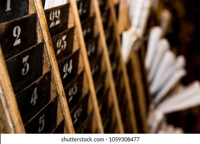 Numbered Old And Faded Time Clock Punch Card Wall Rack With Papers In The Distance