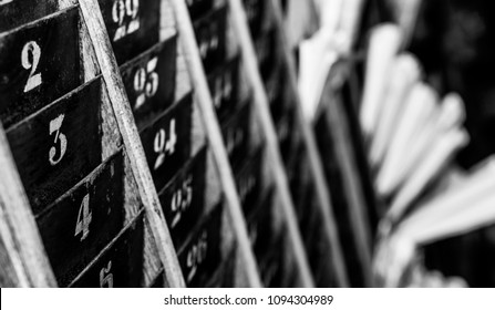 Numbered Old And Faded Time Clock Punch Card Wall Rack With Papers In The Distance