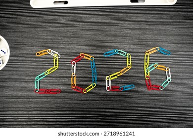 The numbers 2026 are creatively arranged using vibrant, multicolored paperclips against a dark