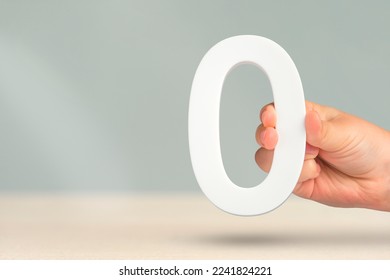Numeral zero in hand. A hand holds a white number zero on a blurred background with copy space. Zero concept, 0 percent interest rate, minimum air emissions, cost or credit no increase.