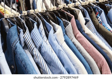 Numerous collared shirts with varied patterns and solid colors neatly hanging on a display rack