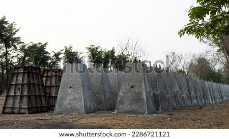 Numerous concrete pillar bases, which were built by cement casting in a steel box and lined up in rows, are left to dry on the ground in rural Thailand, waiting to be buried and assembled.