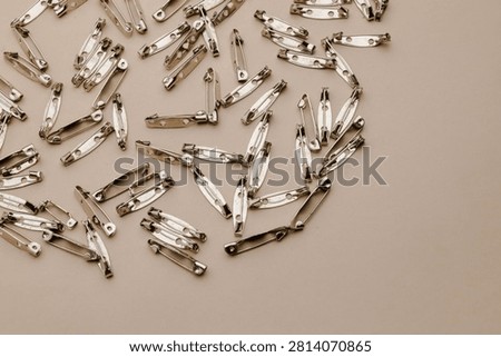 Numerous small silver-colored fasteners, resembling badge or brooch components, lie scattered across a neutral beige background. The mood is minimalist, clean, and inspiring for creative work, ideal for craft blogs, product packaging, or industrial design concepts