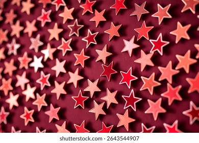 Numerous small, star-shaped objects in varying shades of red and pink are arranged in a repeating pattern against a deep maroon backdrop.