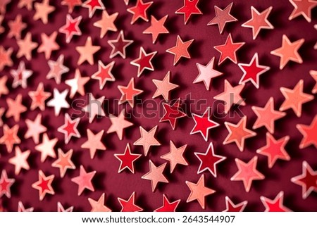 Numerous small, star-shaped objects in varying shades of red and pink are arranged in a repeating pattern against a deep maroon backdrop.