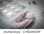 Numismatics. Old collectible coins made of silver on a wooden table.  A collector in special gloves holds an old coin.