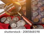 Numismatics. Old collectible coins made of silver on a wooden table.Coins in the album.Collection of old coins. Magnifying glass