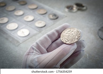 Numismatics. Old collectible coins made of silver on a wooden table.  A collector in special gloves holds an old coin.