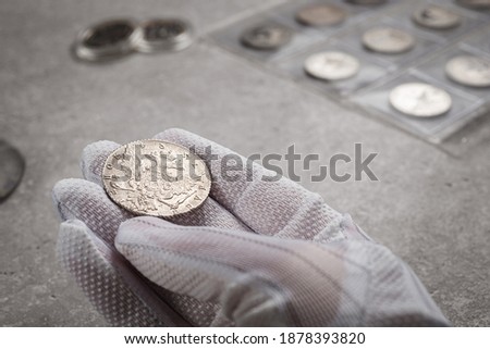 Numismatics. Old collectible coins made of silver on a wooden table. A collector in special gloves holds an old coin.